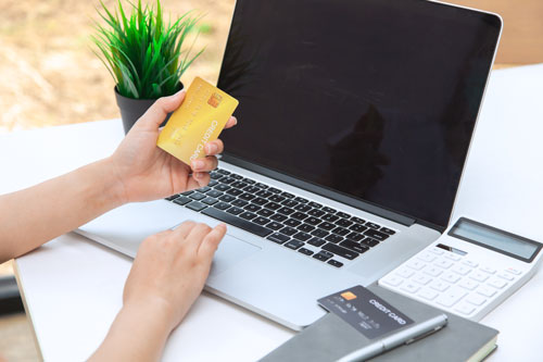 Symbolbild Person an Laptop mit Kreditkarte in der Hand